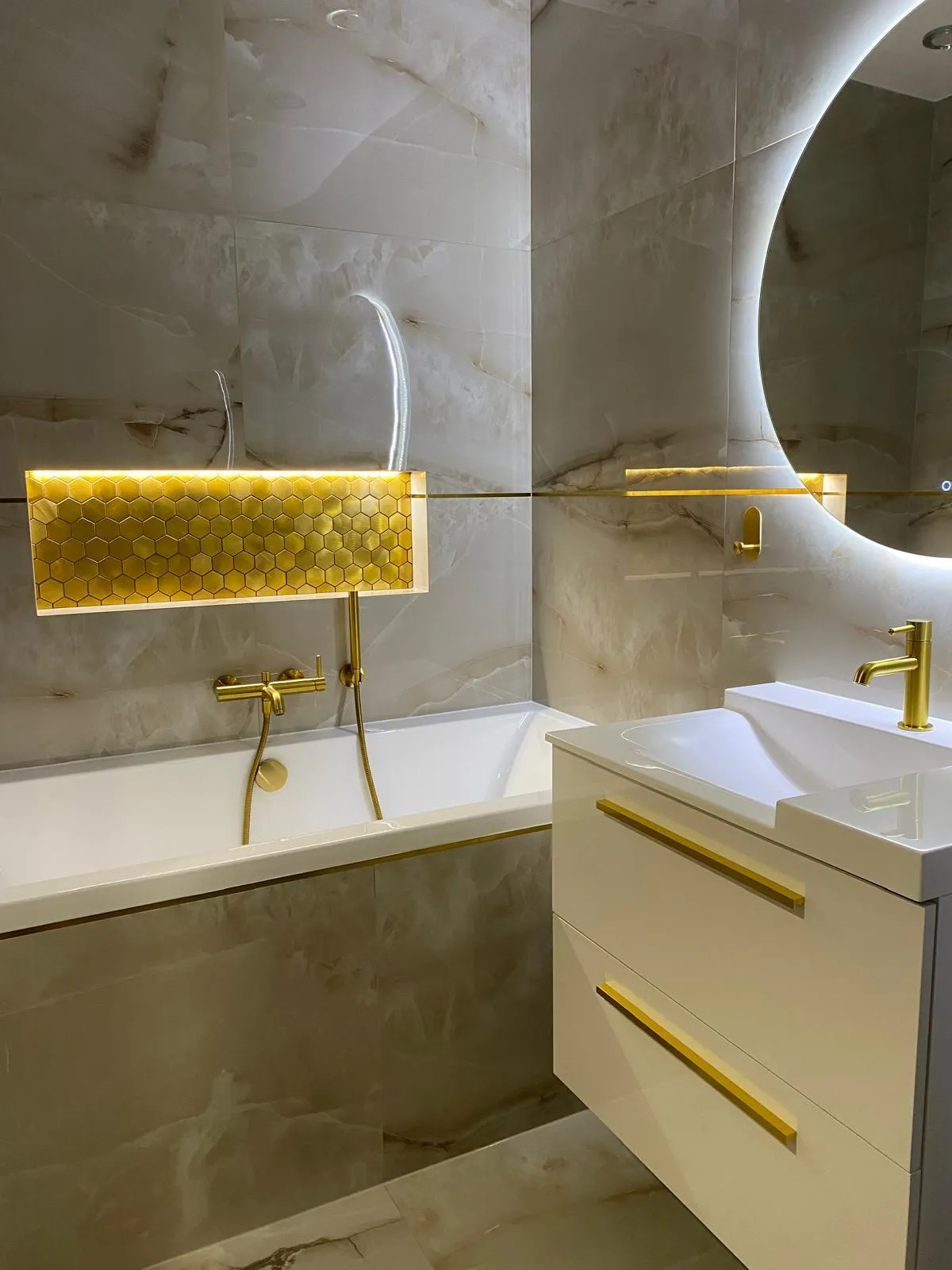 Badezimmer mit goldenen Armaturen und beleuchtetem Spiegel in Marmoroptik