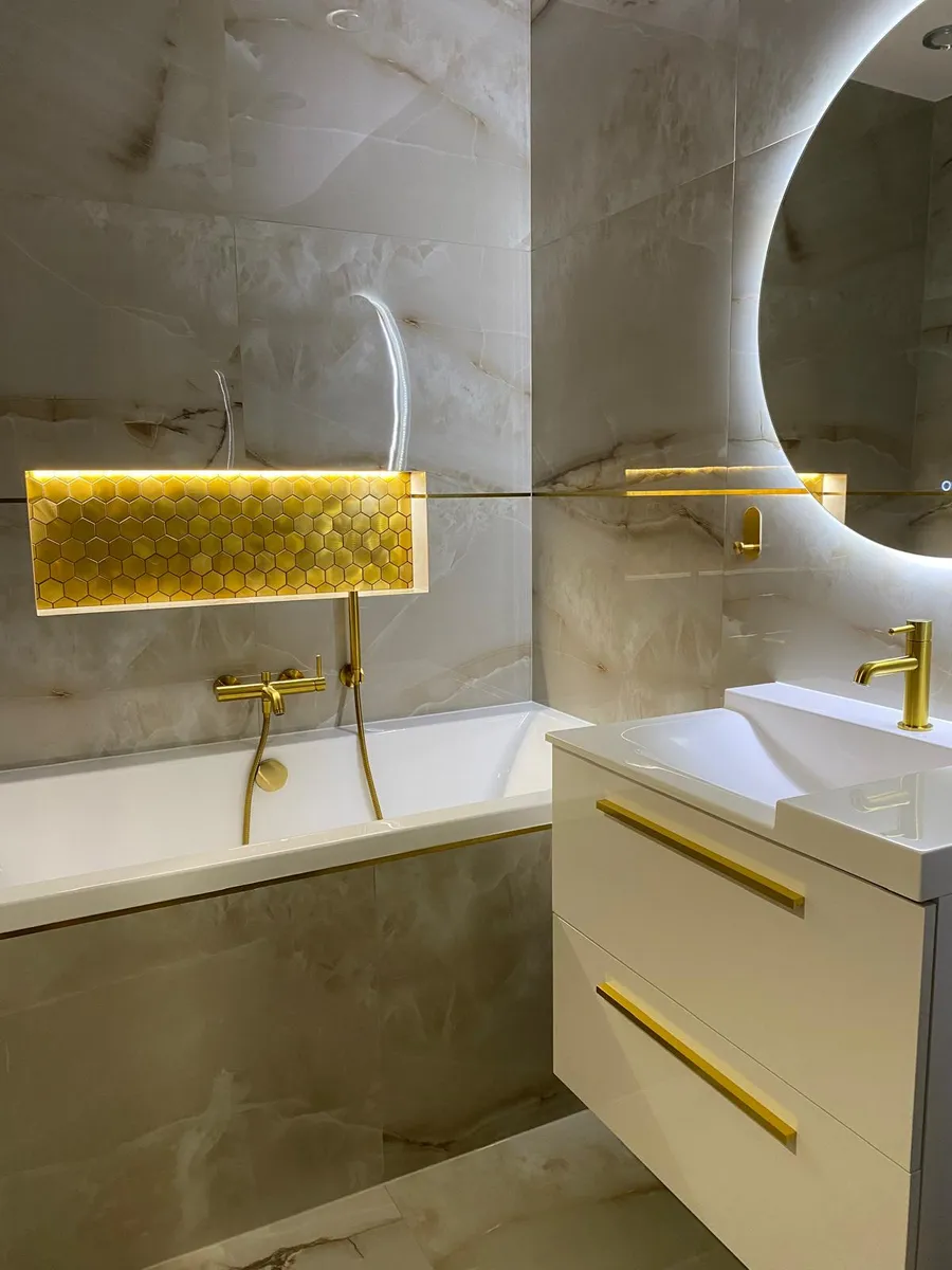 Badewanne und Waschtisch mit goldenen Armaturen in Marmoroptik