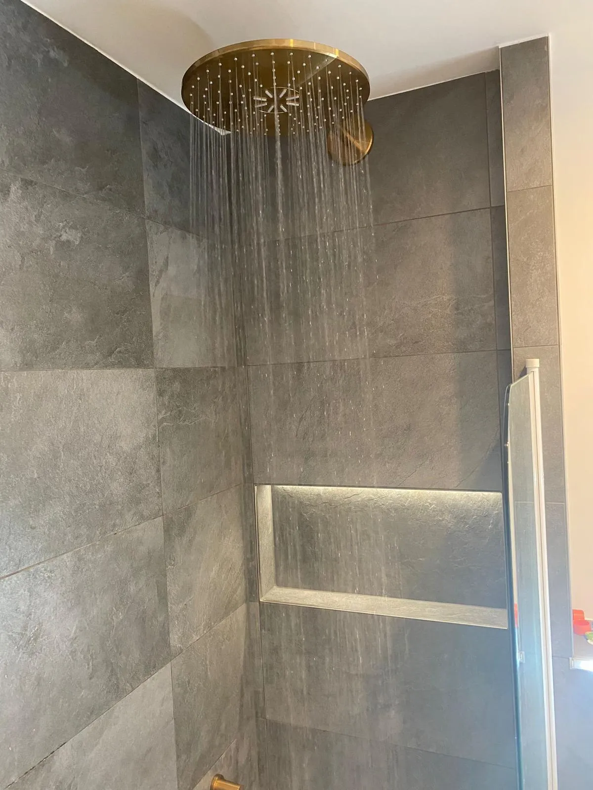 Fertige Dusche mit goldener Regenbrause und Großformatfliesen