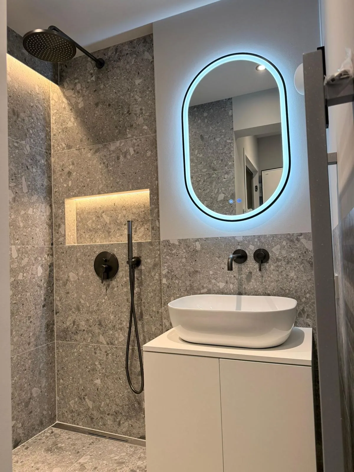Fertiges Bad in Terrazzo-Optik mit ovalem LED-Spiegel und schwarzen Armaturen