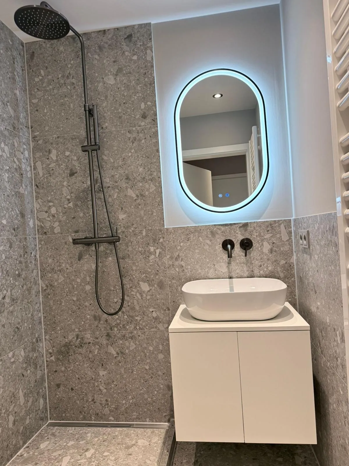Bad in Terrazzo-Optik mit bodengleicher Dusche, ovalem LED-Spiegel und Aufsatzwaschbecken
