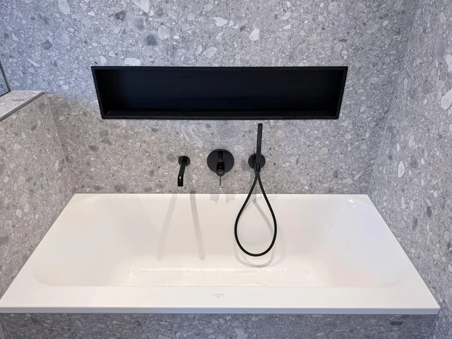 Eingebaute Badewanne in Terrazzo-Optik mit schwarzer Wandnische und Armatur