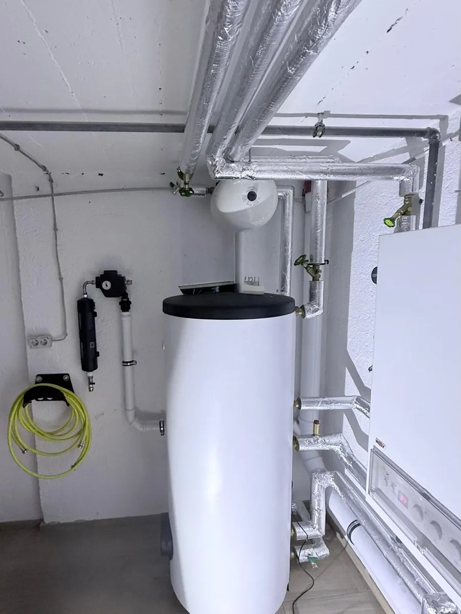 Heizungsraum mit Wandheizgerät, Warmwasserspeicher und gedämmten Heizungsleitungen